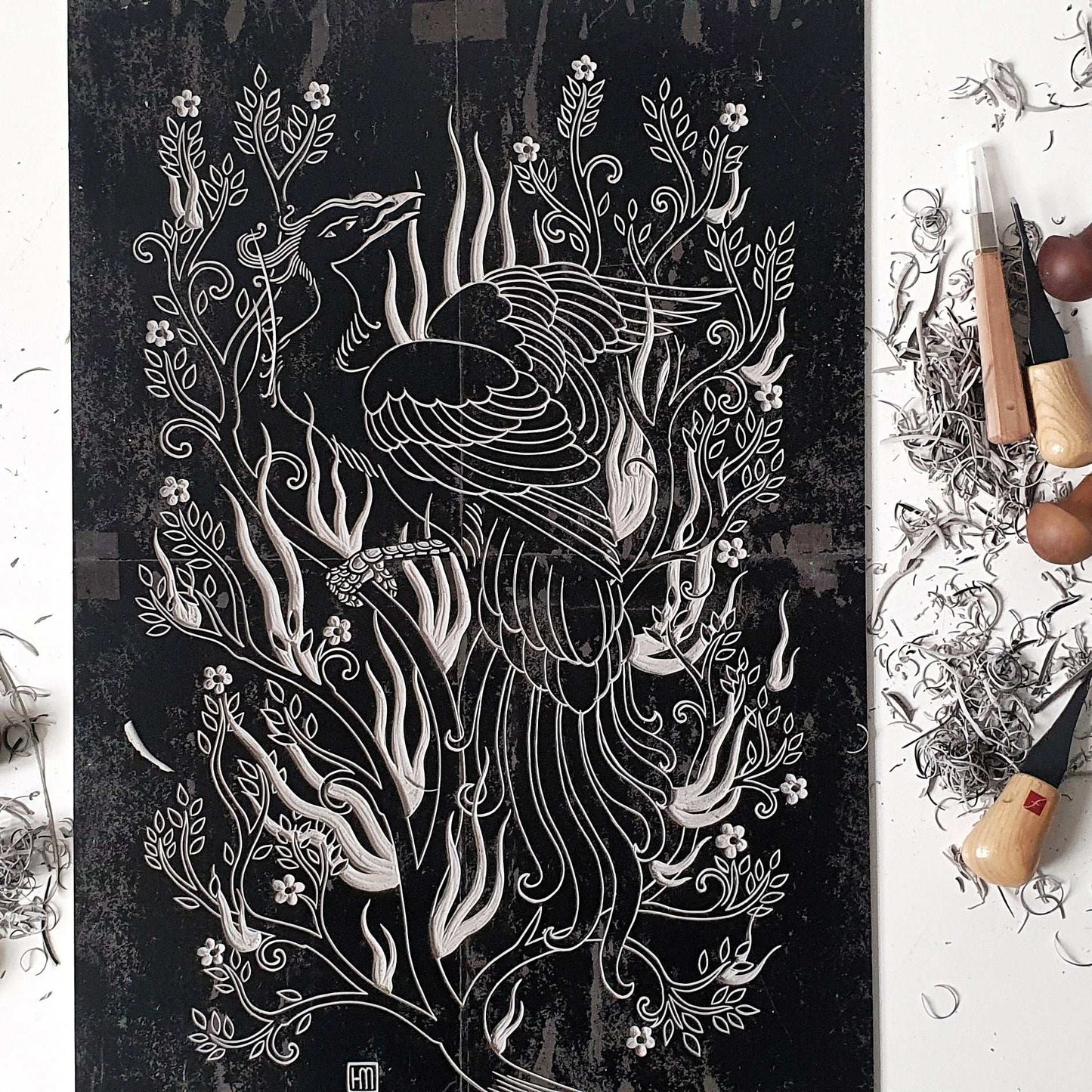 Hand carved linocut printing block next to different size gouges