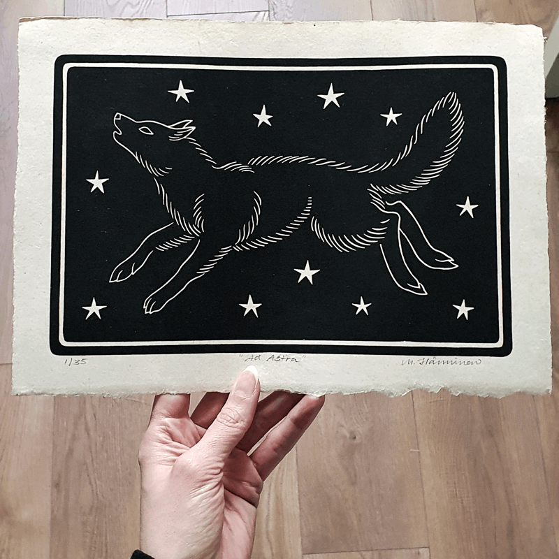 Hand holding a linocut print of a wolf against a starry sky