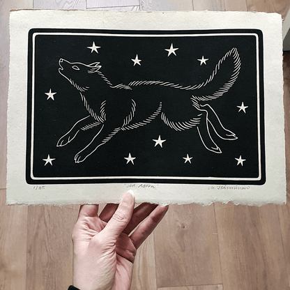 Hand holding a linocut print of a wolf against a starry sky