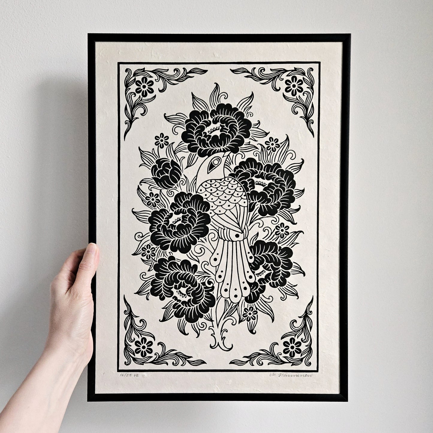 Hand holding a framed relief print of a bird and peony flowers printed in black on white paper