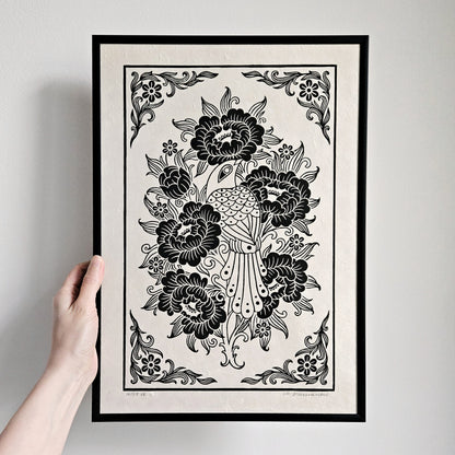 Hand holding a framed relief print of a bird and peony flowers printed in black on white paper