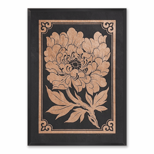 A framed linocut print of a golden peony on black paper