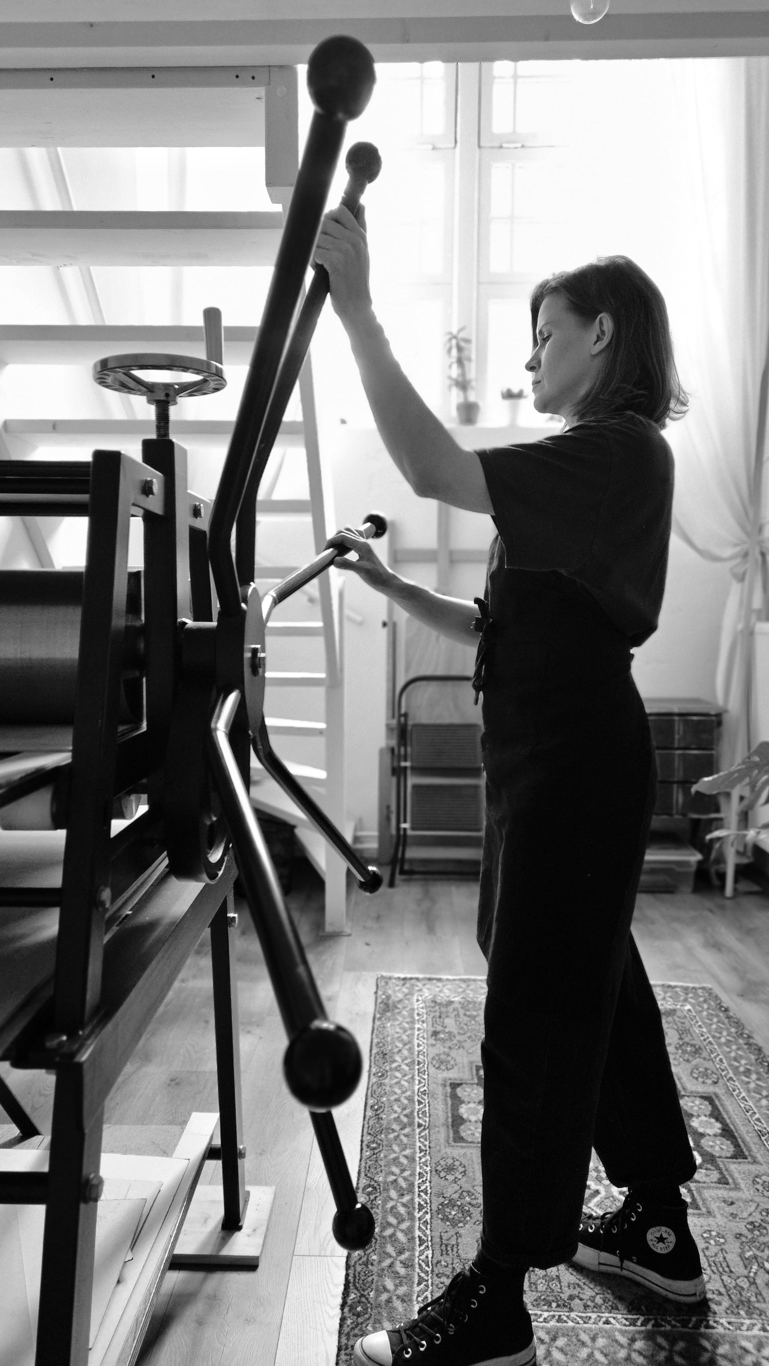 Person operating a large printing press in a room with large windows.