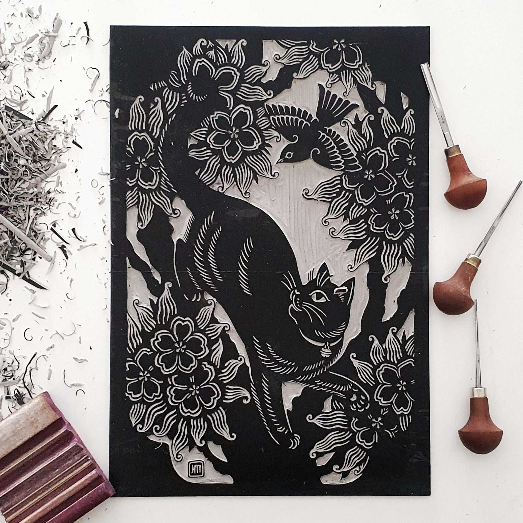 Hand carved linocut block of a cat next to linocut tools