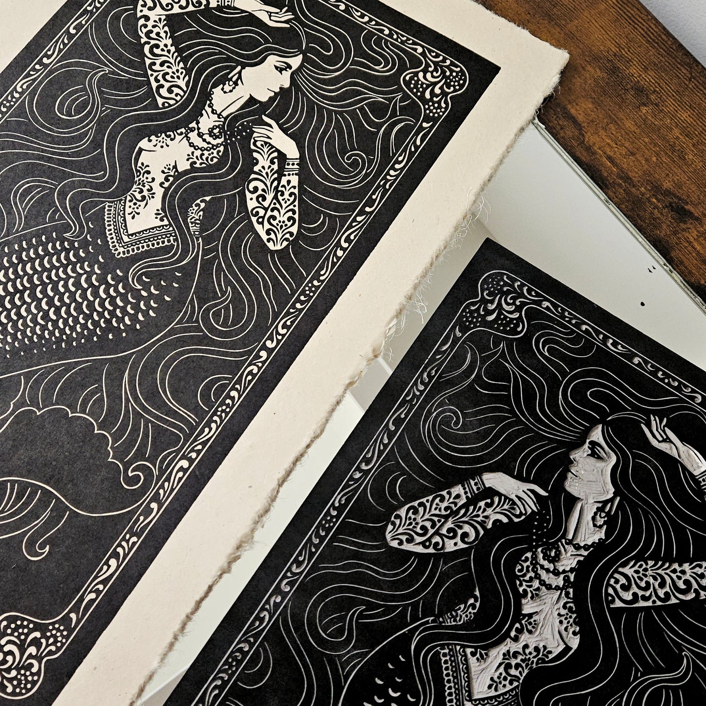 A black and white art prints and linocut block of a siren with intricate patterns on a wooden surface.