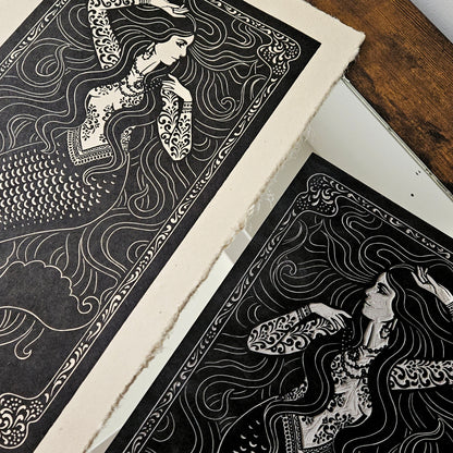 A black and white art prints and linocut block of a siren with intricate patterns on a wooden surface.